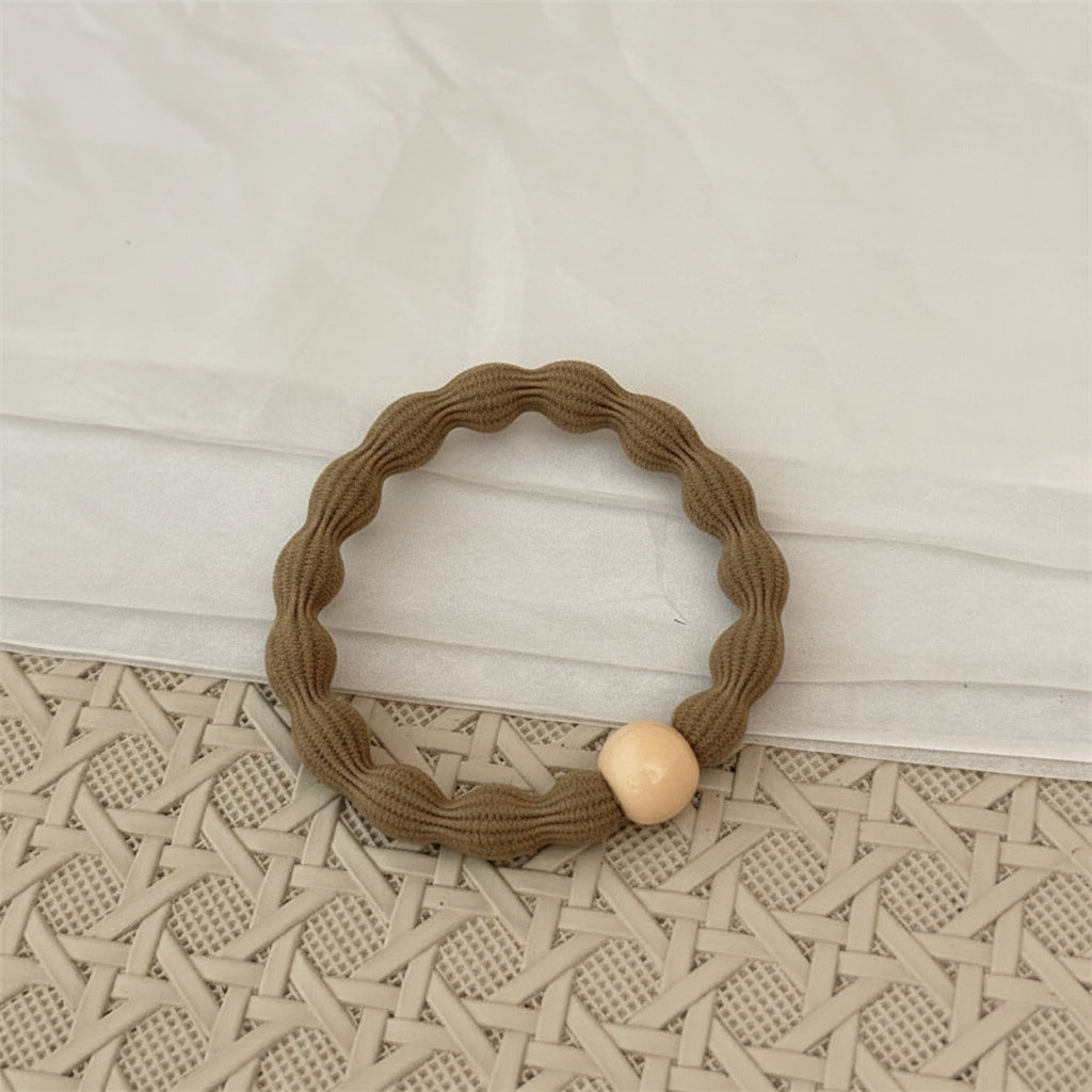 Brown woven hair tie with a beige bead on a textured surface